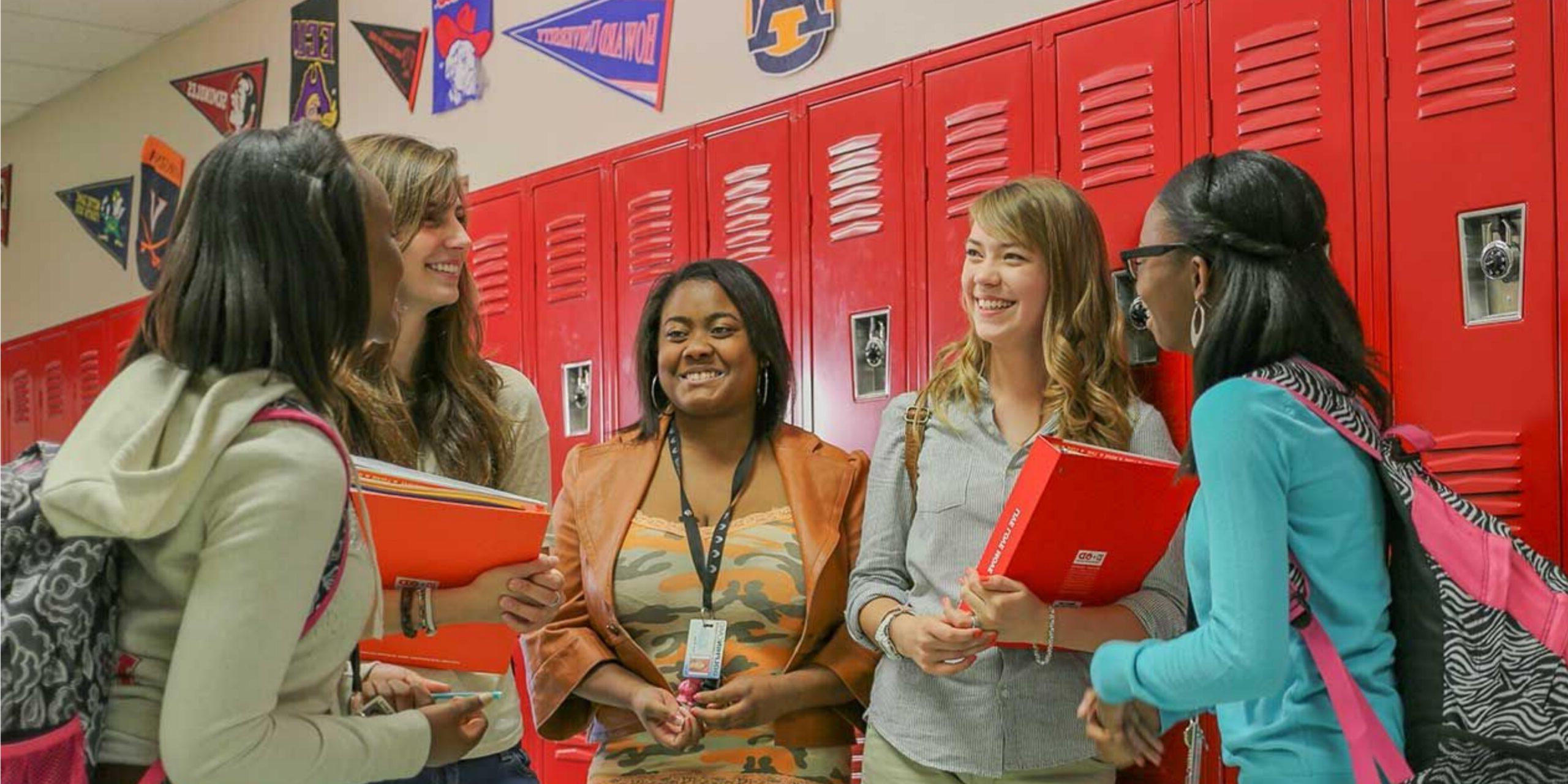high school students chatting in the hall in front of red lockers